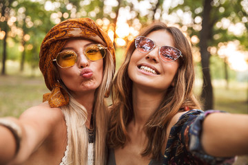 Photo of two european hippie women, smiling and taking selfie while walking in forest