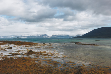 scenic shot of lake shore in Iceland with snowy mountains on background