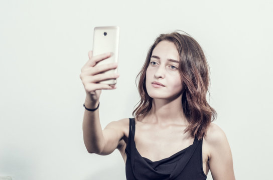 Beautiful young girl holding a phone. Makes photos, selfies