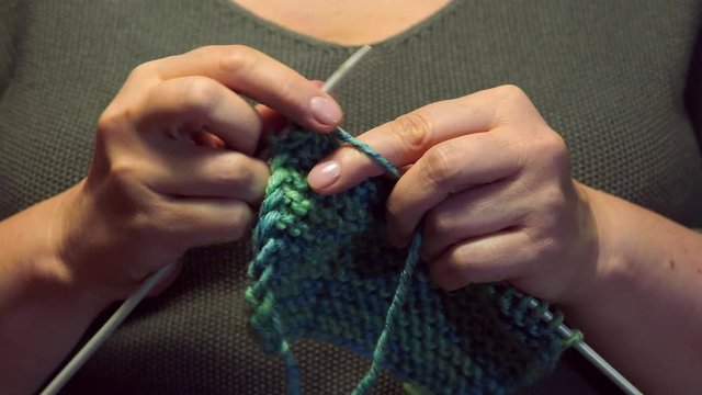 female hands knit a scarf close up under warm electric light