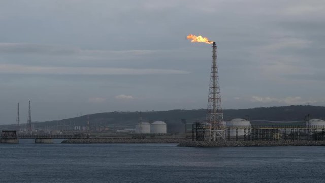 Flare stack of petrochemical refinery on sea shore in evening