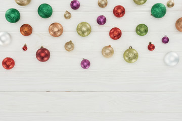 top view of beautiful shiny colorful christmas balls on white wooden background