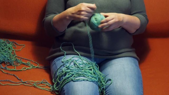 woman winds a ball of yarn under warm electric light