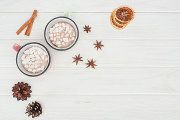 Fototapeta na wymiar flat lay with cups with hot chocolate and marshmallows, cinnamon sticks and pine cones on wooden table