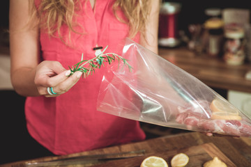 Close up of woman adding rosemary while preparing sous vide meal.