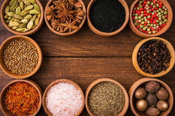 Spices on a wooden background in bowls, frame, place of copying, seasoning, saffron, cumin, black sesame, cardamom, nutmeg, pink salt, star anise, coriander