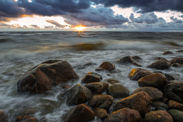 A sea landscape with rocks, a storm and a setting sun. Waves, rocks, storm and clouds.
