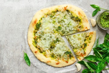 Homemade Pesto pizza sliced with fresh basil leaves top down view