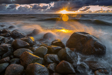 A sea landscape with rocks, a storm and a setting sun. Waves, rocks, storm and clouds.
