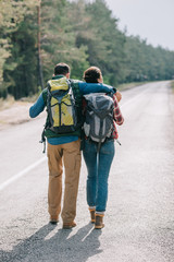back view of couple of travelers with backpacks walking on road