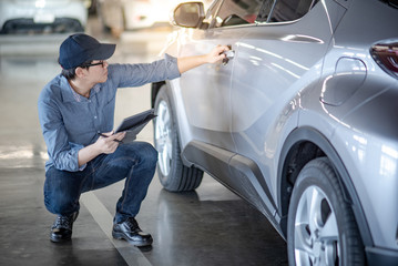 Asian auto mechanic holding car door handle and digital tablet checking the car in auto service garage. Mechanical maintenance engineer working in automotive industry. Automobile servicing and repair