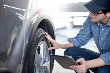 Fototapeta na wymiar Young Asian auto mechanic holding digital tablet checking car wheel in auto service garage. Mechanical maintenance engineer working in automotive industry. Automobile servicing and repair concept