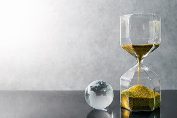 Reflection of gold sand running through the shape of hourglass with world globe crystal glass on...
