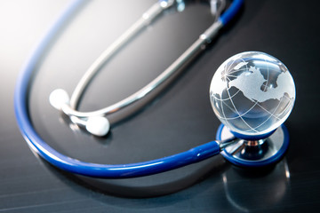 Global healthcare concept. World globe crystal glass on blue stethoscope on glossy desk. Health and medical science. Worldwide wellness business