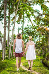 Fototapeta premium Young honeymoon couple walking among rice fields. Beautiful trip of newleds to Bali island, Indonesia. Nature, summer, green, bright.