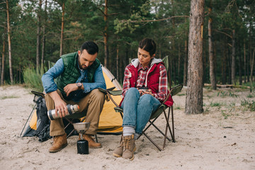 couple having camping on sandy beach with pine forest behind