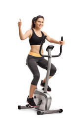 Obraz premium Young female riding a stationary bike and showing thumb up