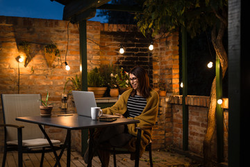 Woman working late on laptop in her backyard
