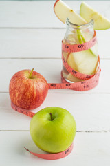 Green and red apples in soda bottle with measuring tape on white table