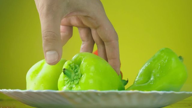 Fresh Balgar peppers fall with water on a plate. The concept of nutrition. Isolate on a yellow background, slowdown.