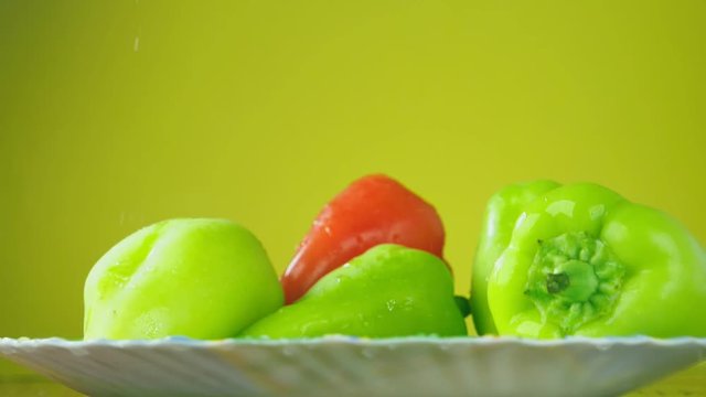 Fresh Balgar peppers fall with water on a plate. The concept of nutrition. Isolate on a yellow background, slowdown.