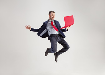 Image of young surprised man over white studio using laptop computer while jumping. illumination in...