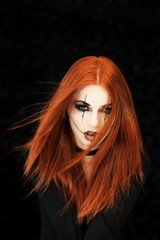 Beautiful, young woman with halloween make up and red hair poses in front of black background