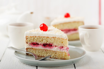 Slice vanilla cake with butter cream icing in the plate on white wooden table.