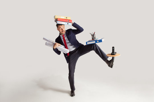 Young businessman in a suit juggling with office supplies in his office, isolated on white background. Conceptual collage with phone, folders. The business, office, work concept.