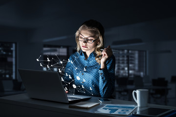 Attractive blonde wearing glasses in dark office using laptop. M