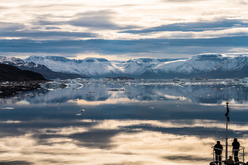 Leute, die auf dem Boot des Expeditionsschiffes stehen und massive Eisberge beobachten, die im Fjord Scoresby Sund, Ostgrönland, schwimmen?