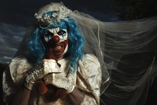 evil clown in bride dress strangling a teddy bear