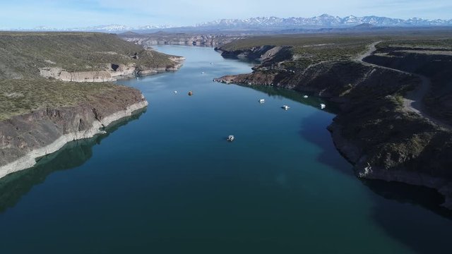 Aerial drone scene of Agua de Toro dam. Flying descending over the lake, passing near boats. Snowy plata mountains at background. San Rafael, Mendoza, Cuyo Argentina.