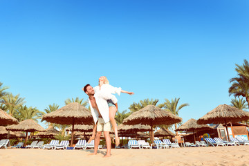  Beautiful young couple having vacation on a sunny beach walking while holding hands, hugging, and taking selfies.  Happy handsome man and blonde woman in white shirts enjoying their trip to hawaii. © Антон Зимин