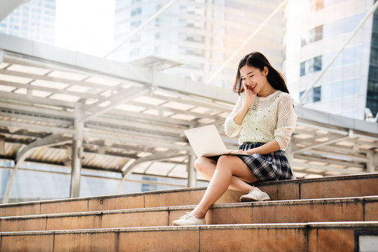 Portrait of a beautiful Asian teenage girl Sitting play on laptop stairs in the big city Looking for learning information. Researching a variety of information. Including online shopping for women.