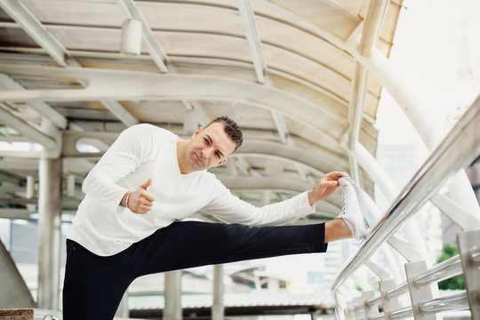 Portrait Of A Man Wearing A Sport In The Big City Exercising To Stretch The Leg Muscles. And In Another Part. In Order To Give Time To Play Sports, Not To Cause Inflammation. To Have A Healthy Body.