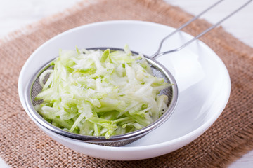 Bowl of grated zucchini on a white background