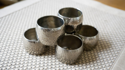 Silver metal napkin rings holders over a golden color place mat. Ready for table setting in an event, party or holiday