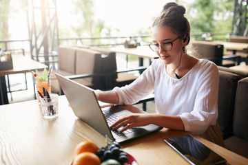 Businesswoman working remotely at cafe with headset and laptop. Mixed race female performing...