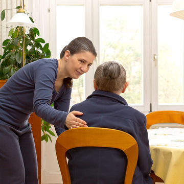 Rear view of a senior woman sitting at home talking to a younger woman from a domestic care service who is helping her during the day, text space