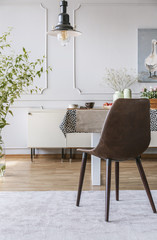 Black chair on grey carpet at table in dining room interior with lamp and wall with molding. Real photo