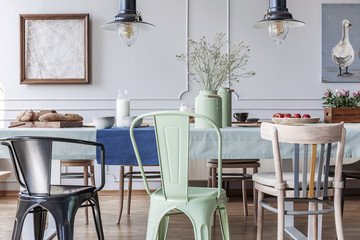 Colorful chairs at table in cottage grey dining room interior with lamps and posters. Real photo