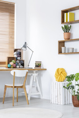 Knitted pillow next to a wooden desk in a teenager room interior