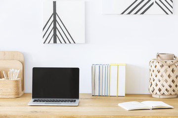 Close-up of a laptop on a desk next to a notebook and books in a home office interior. Empty screen, place your graphic