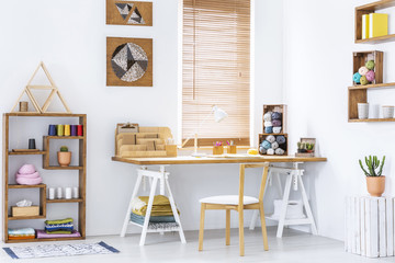 Real photo of a creative room interior with a desk, shelf and knitting wool