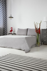 Elegant bedroom interior in gray with red accents of fresh gladiolas and an accessory. Bed with...