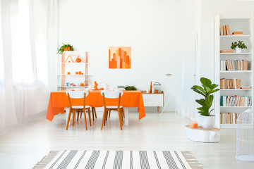 Real photo of dining room in vivid color. Orange tablecloth on long table with white chairs