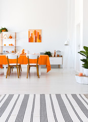 Vertical view of living room with long table, chairs and orange details. Real photo concept