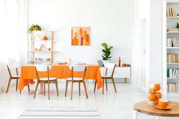 White and orange dining room with painting on the wall, bookshelf in the corner and green plant in the pot