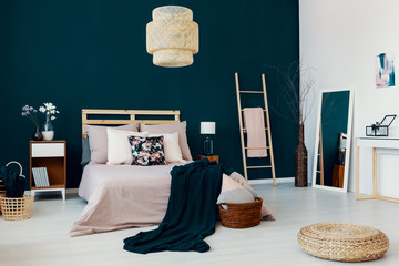 Real photo of bright bedroom interior with double bed, flowers and books on bedside table, dark...